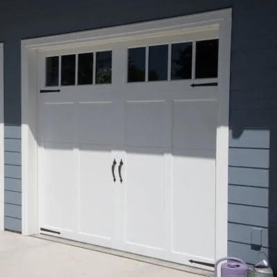 White two-section garage door with black hardware and glass panels on residential home