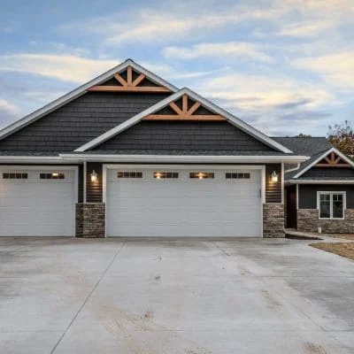 White raised-panel garage doors on modern residential home with stone accents and timber framing