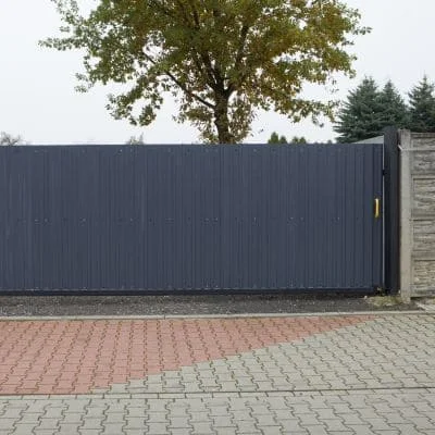 Dark gray corrugated metal sliding gate with stone pillar support on brick paver driveway