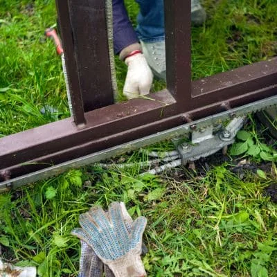 Technician servicing sliding gate track and hardware with cleaning tools on grass