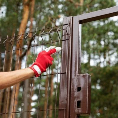 Technician installing metal gate with wire mesh fencing and locking hardware
