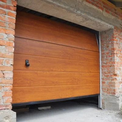 Honey-stained wood garage door with horizontal panels and black trim in brick opening