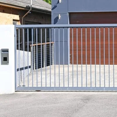 White aluminum automated driveway gate with vertical slats and brick privacy screen