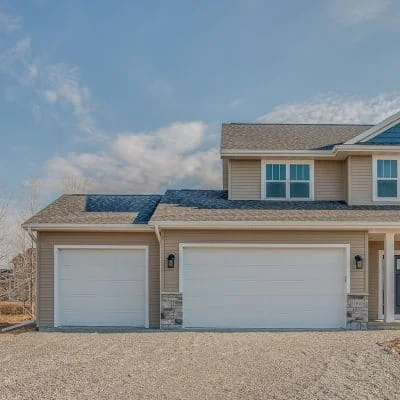 Two white raised-panel garage doors on residential home with stone pillars and vinyl siding